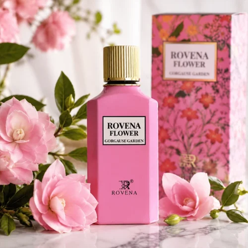 عطر ROVENA FLOWER صورتی با درب طلایی در میان گل‌های صورتی و سفید و شاخه‌های ظریف، با پس‌زمینه صورتی روشن